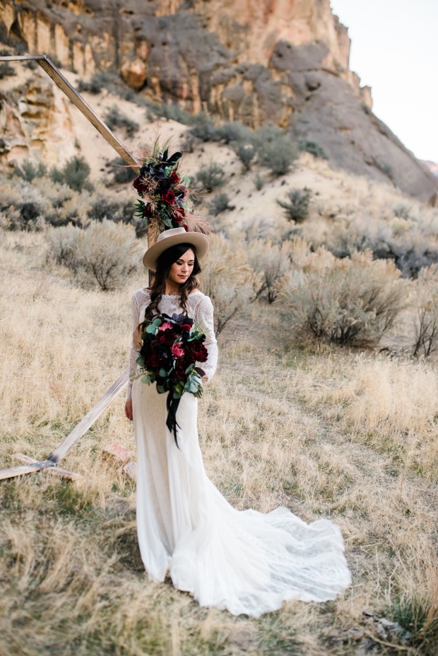 Bride in white gown with dark bouquet, desert backdrop