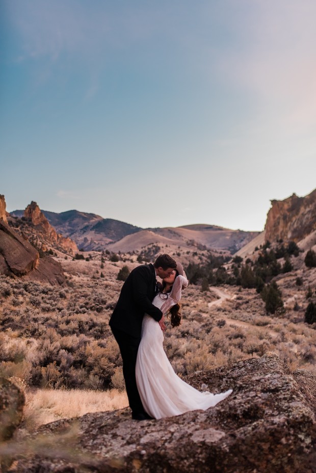 Bride and groom kiss on a rock with a stunning mountain backdrop