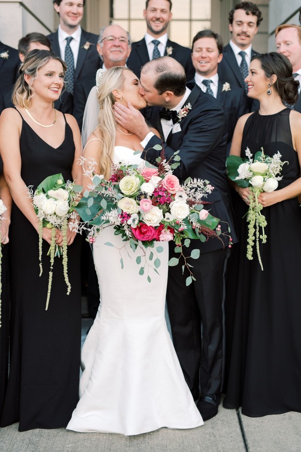 Bride and groom share a kiss at the wedding surrounded by loved ones
