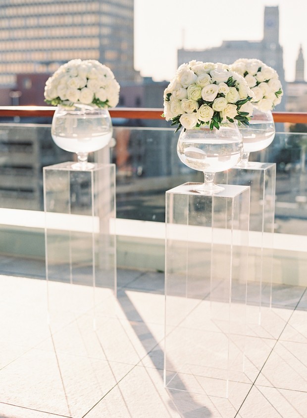 Elegant white floral arrangements on acrylic pedestals outdoors