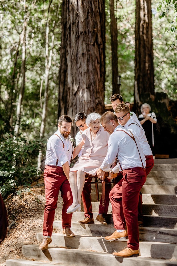 Groomsmen carrying an elderly woman up wooden steps, outdoor wedding