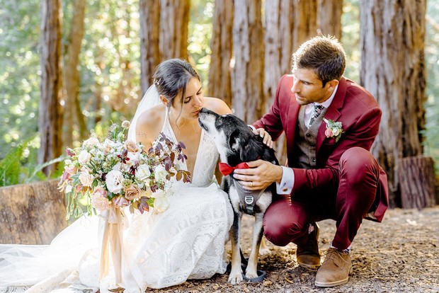 Bride and groom kissing dog at an outdoor wedding ceremony