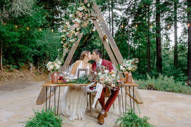 Romantic outdoor wedding kiss with floral arch and table setup