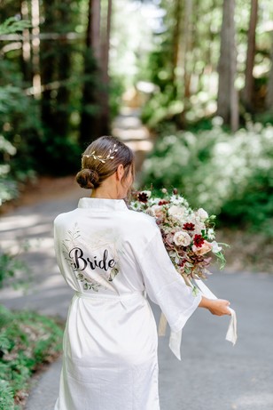Bride in white robe, holding a bouquet, walking on a path