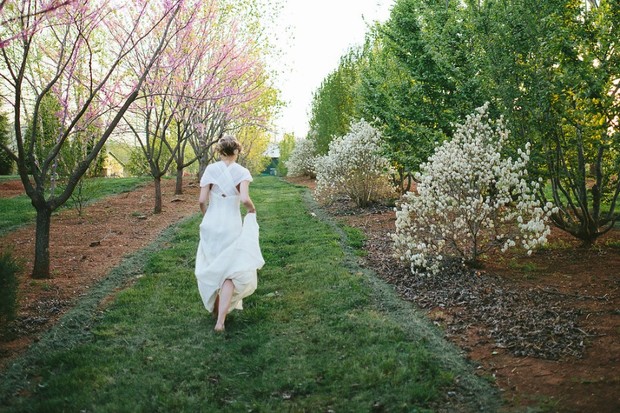 Woman in white dress walks down grassy path between trees