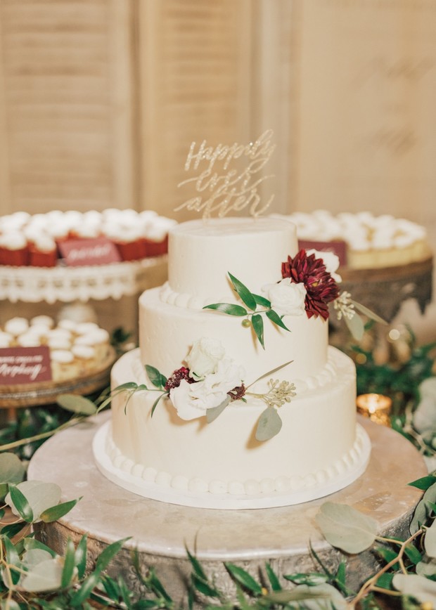 Three-tiered wedding cake decorated with flowers and happily ever after topper
