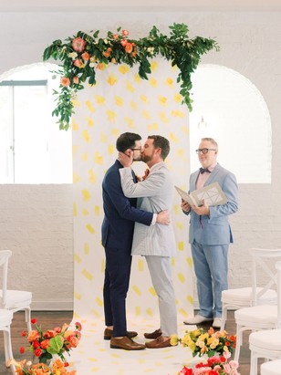Two grooms share a kiss at their charming indoor wedding