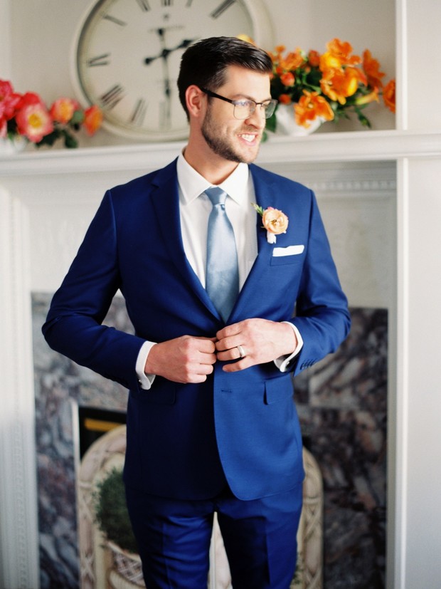 Groom in blue suit buttons his jacket smiling sideways