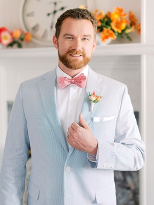 Groom in a seersucker suit and pink bow tie smiling