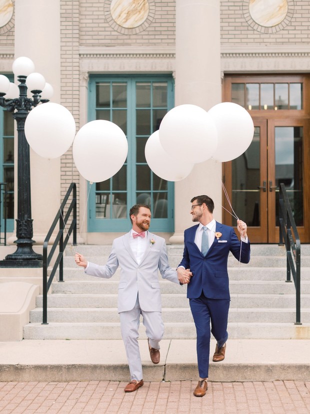 Gay couple holding hands with white balloons on wedding day