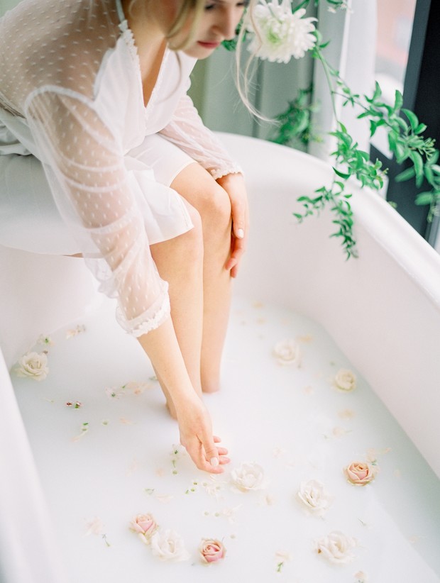 Woman in white robe relaxing in milk bath with flowers
