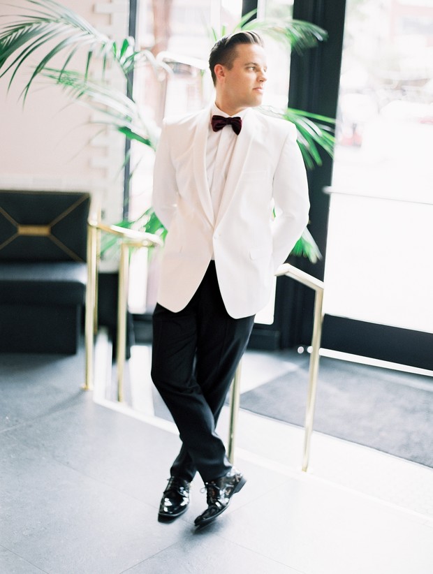 Stylish groom in white tuxedo, black pants, bow tie