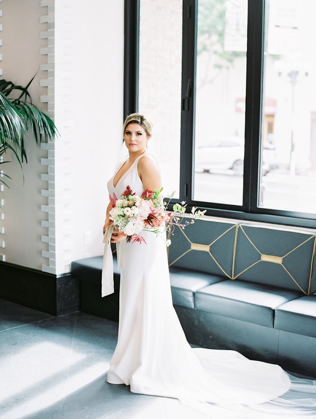 Bride in elegant white gown holding bouquet near window