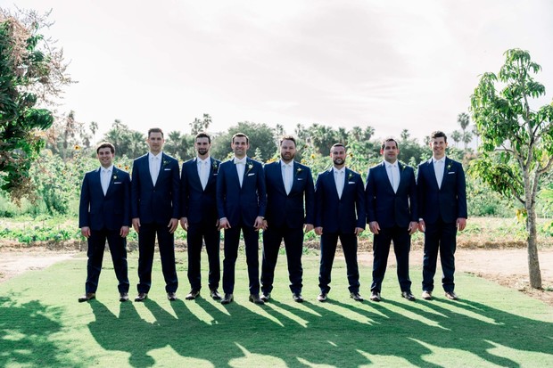 Groomsmen in navy suits pose on the green grass for a wedding photo