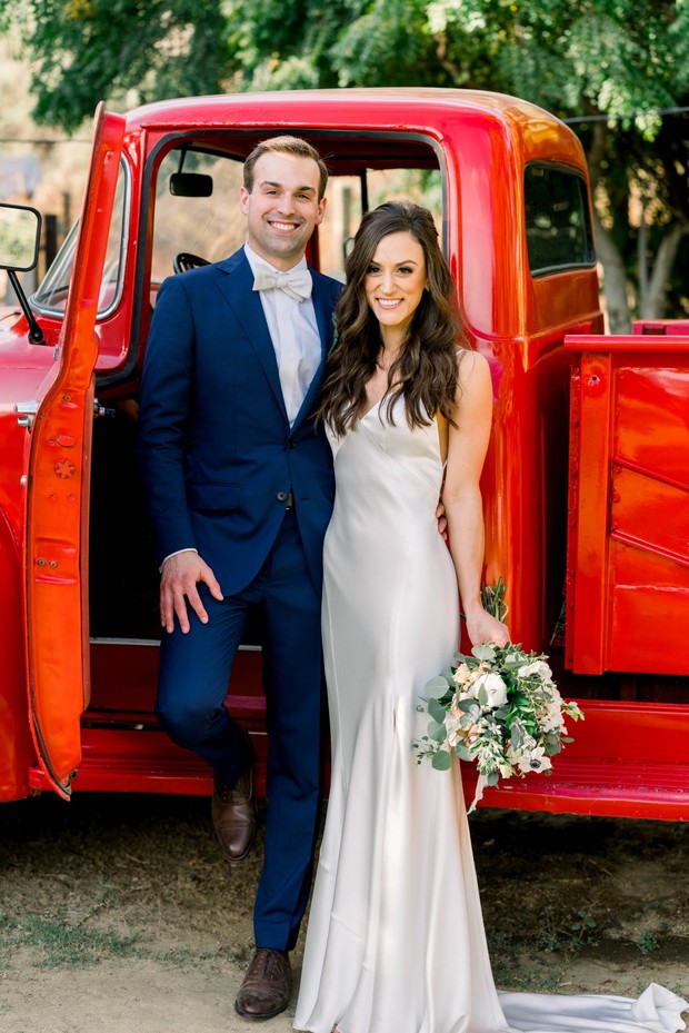 Happy couple posing next to a red truck on their wedding day