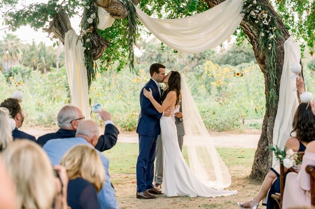 Couple kisses at their wedding ceremony under a tree arch