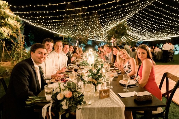 Group of people smiling at a table under string lights at night