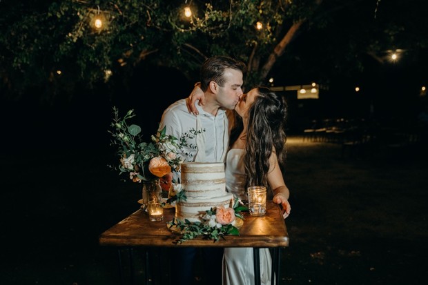 Newlyweds kiss over their wedding cake at night