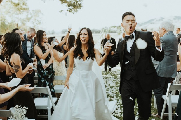 Happy couple exiting wedding ceremony, showered with petals