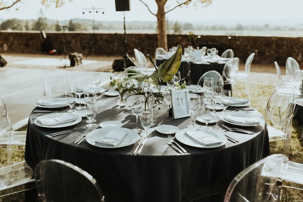 Elegant outdoor event table setting with floral centerpiece and clear chairs
