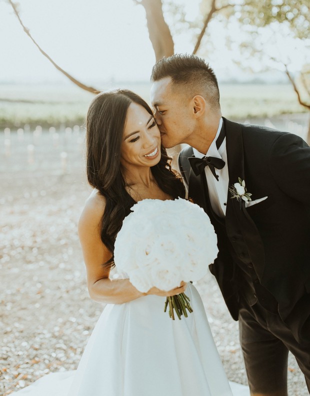 Happy groom kisses bride holding white rose bouquet
