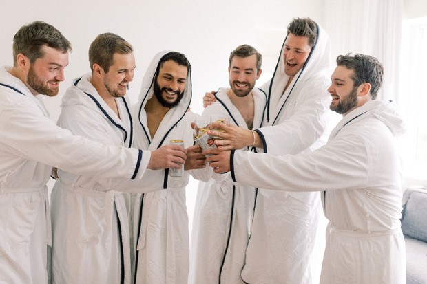 Groomsmen toasting laughing in robes before wedding