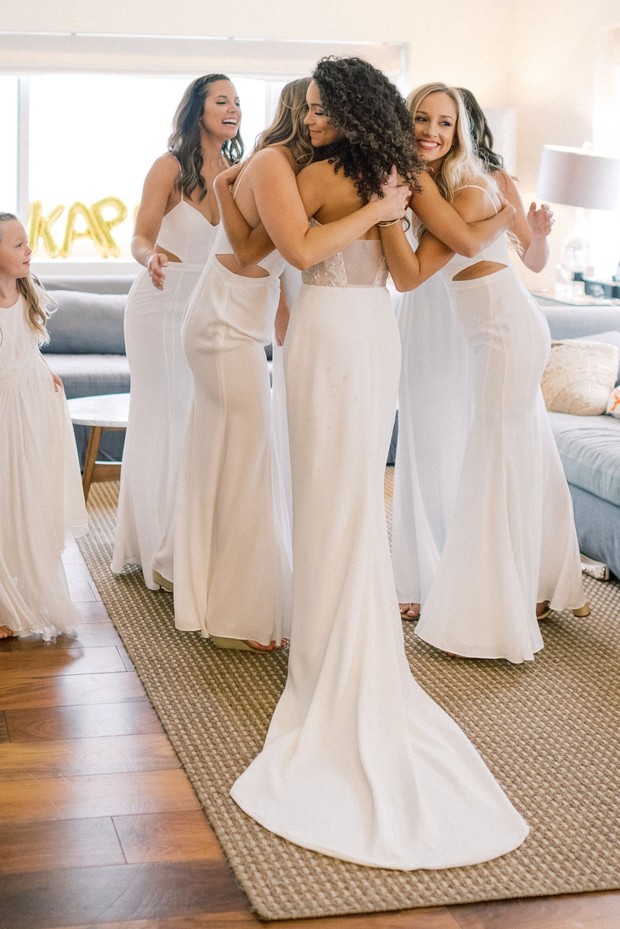 Bride and bridesmaids hug in white dresses before wedding