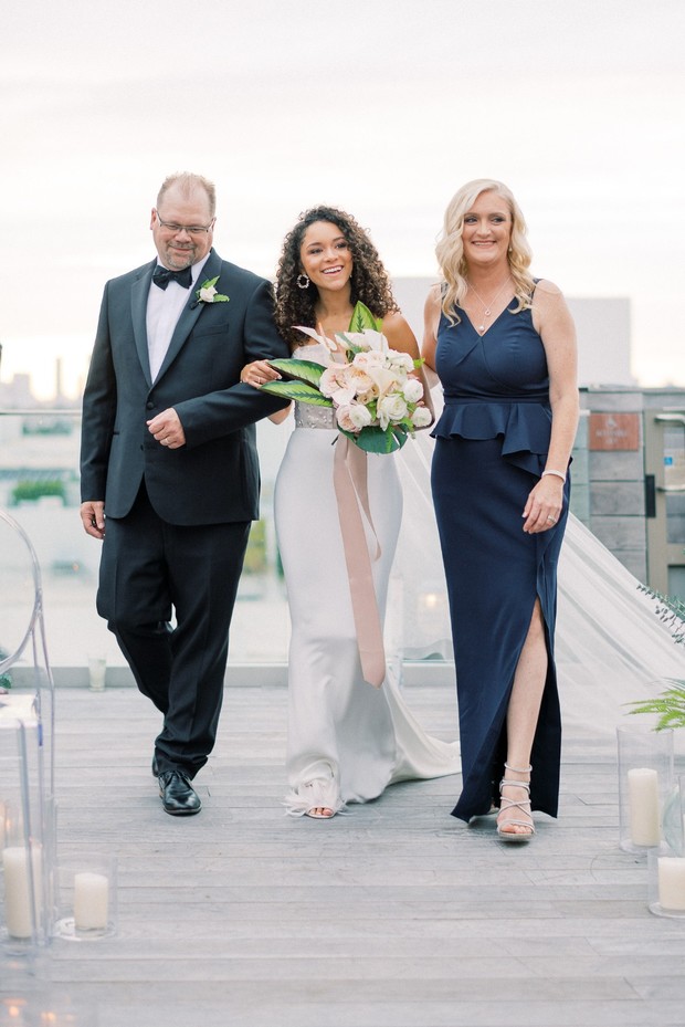 Smiling bride walks with father and mother at wedding ceremony