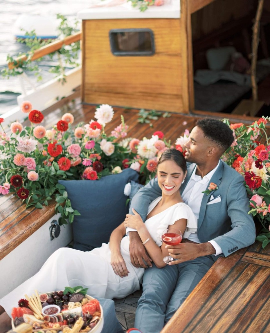 Newlyweds cuddle on a boat adorned with flowers and charcuterie