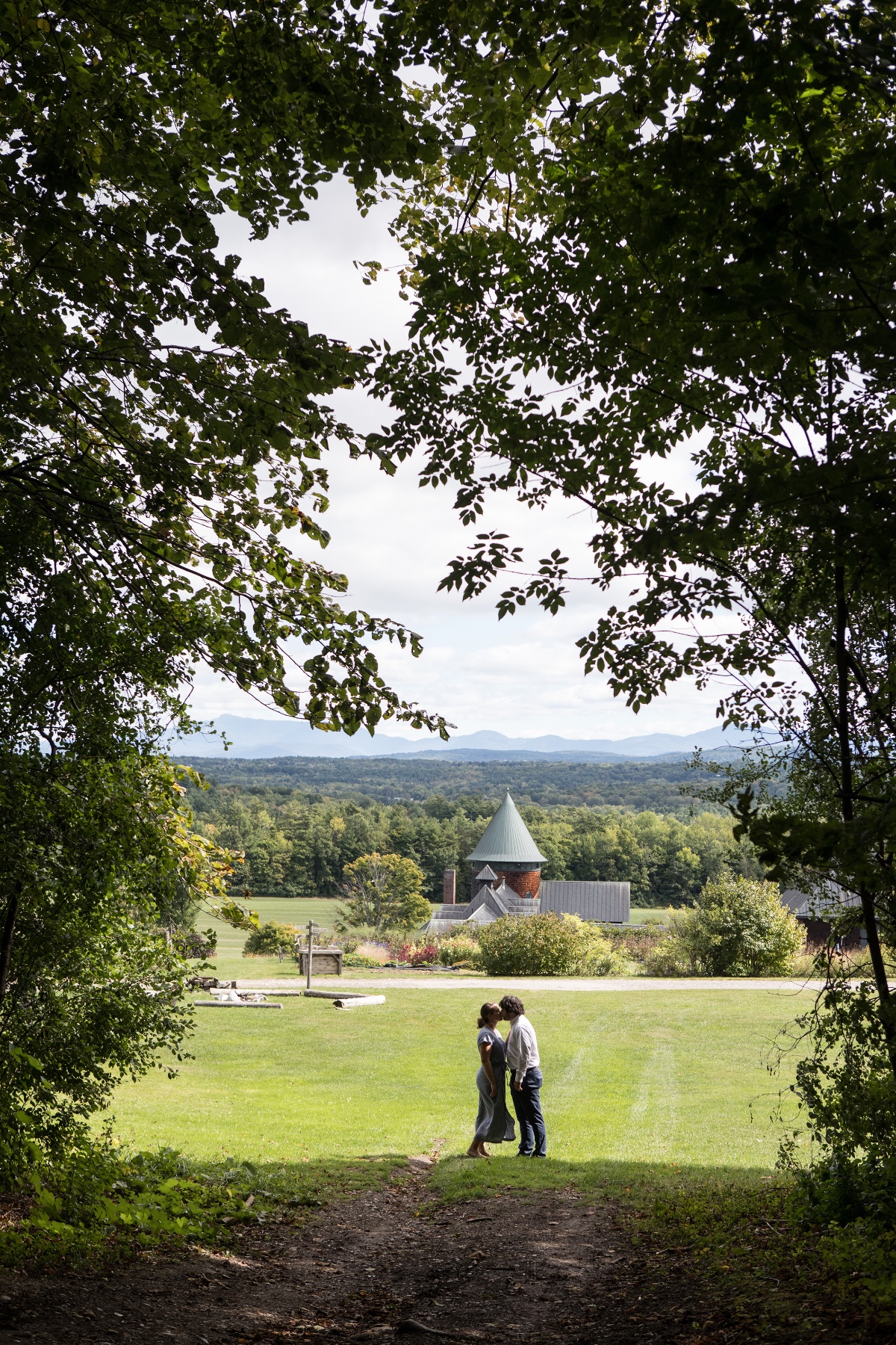 Couple kissing in a field with a scenic view of a distant building