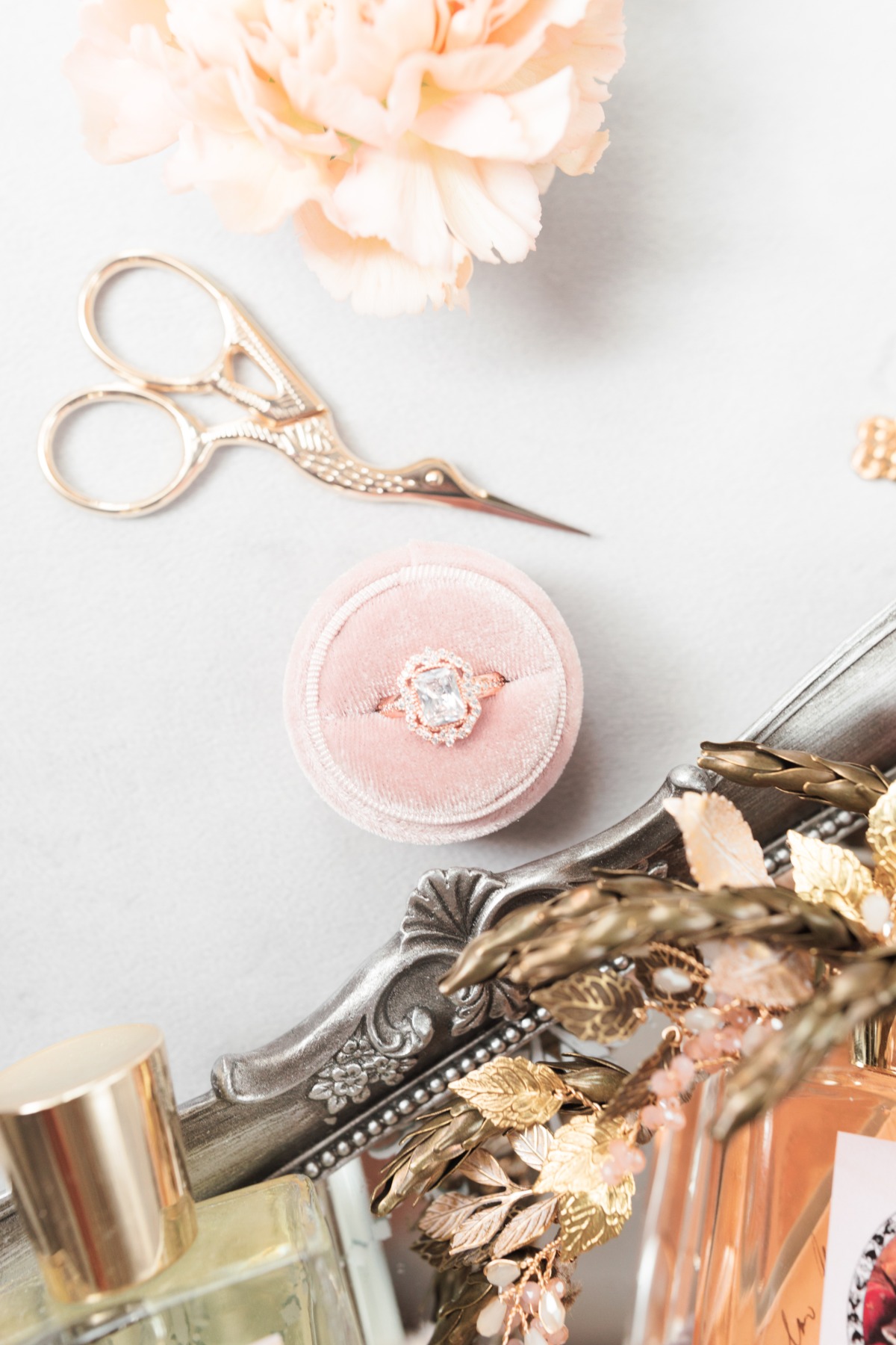 Pink ring box with diamond ring, gold scissors, and perfume