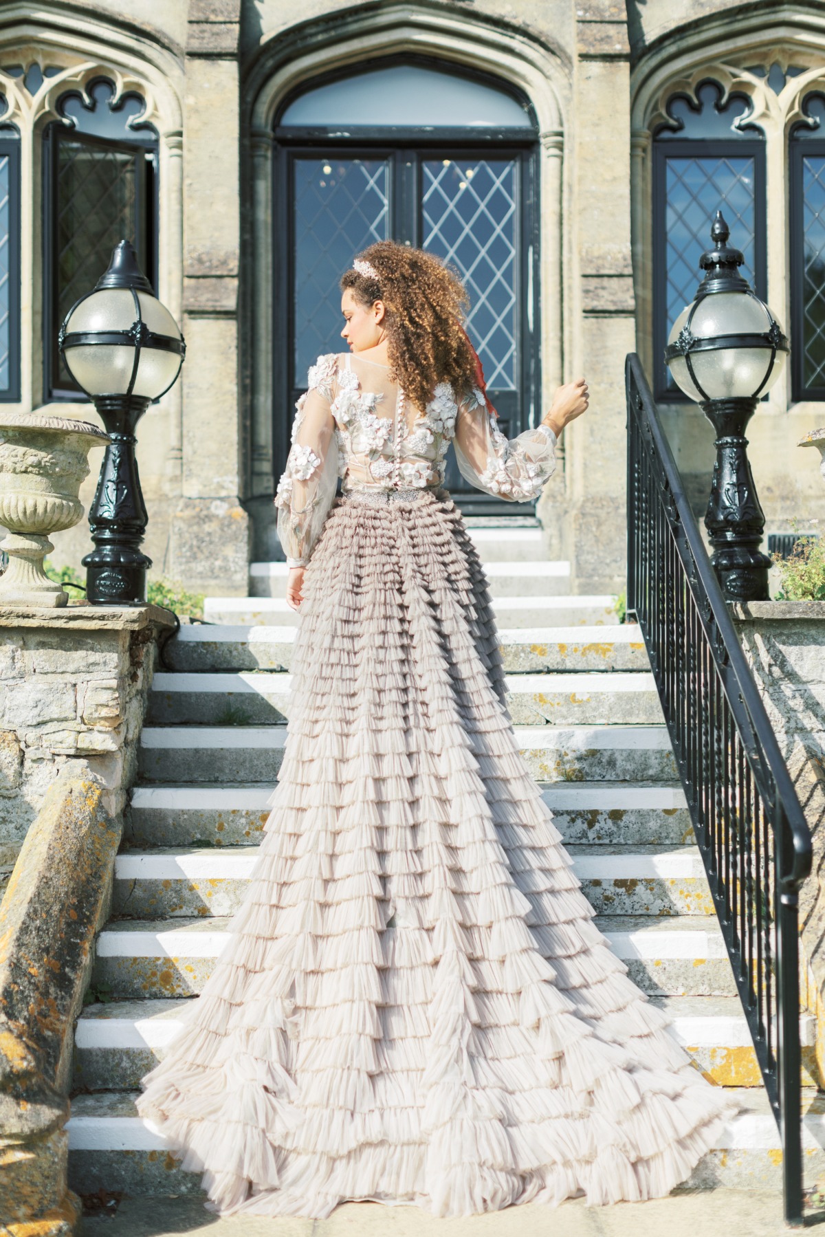Elegant woman in a flowing gown poses on steps of a grand house