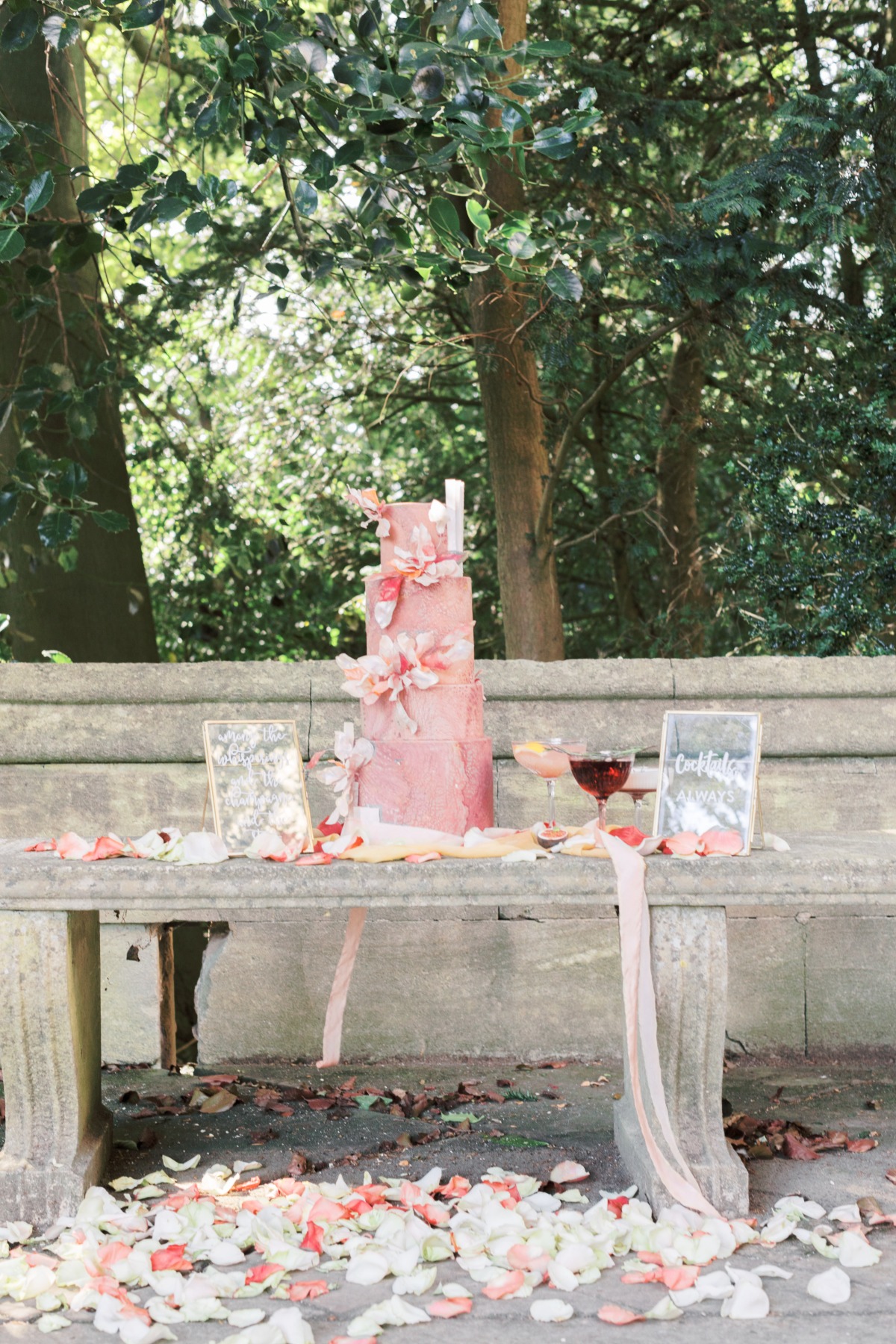 Elegant pink wedding cake with floral decor on a stone bench