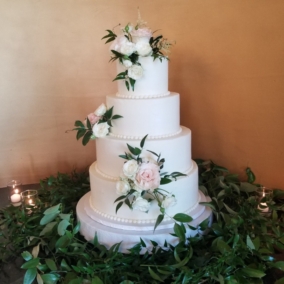 Elegant four-tiered wedding cake adorned with flowers and greenery