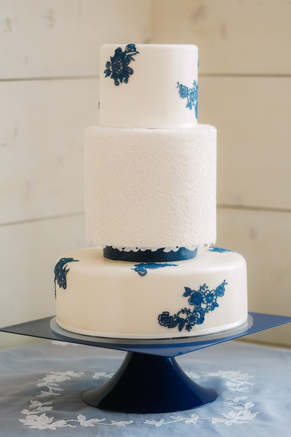 Elegant three-tiered wedding cake with blue floral accents on a stand