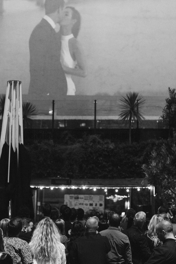 Outdoor movie night scene with a romantic kiss projected on screen