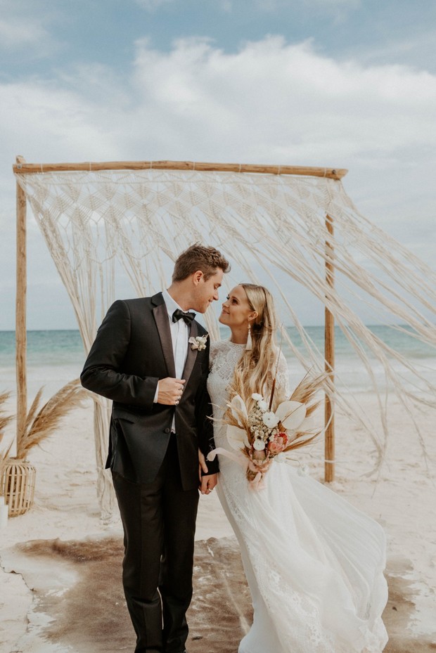 Bride and groom gaze lovingly at beach wedding arch