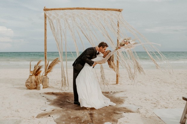 Beach wedding couple shares a kiss under macrame arch