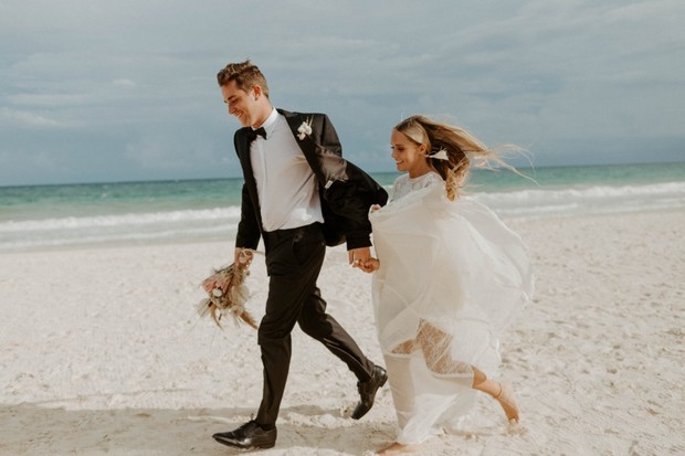 Newlyweds joyfully run on a beach after their wedding