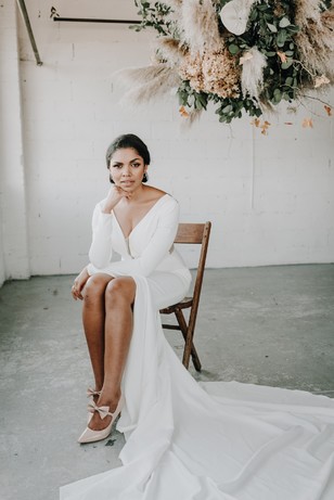 Elegant bride in white gown sits beneath floral arrangement