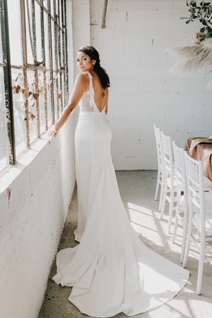 Elegant bride in a sleek wedding dress with a long train by a window