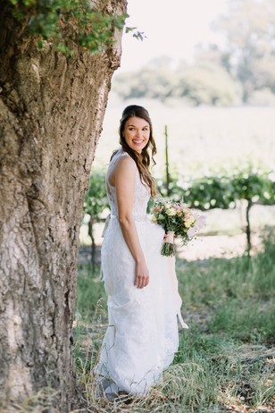 Smiling bride poses by tree holding bouquet outdoors