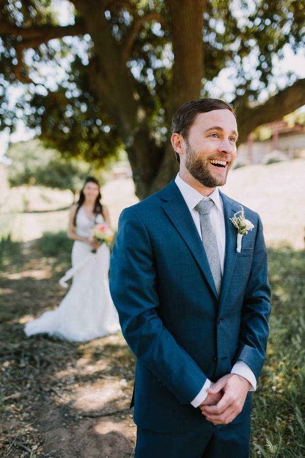 Groom smiles seeing bride walk down the aisle outdoors
