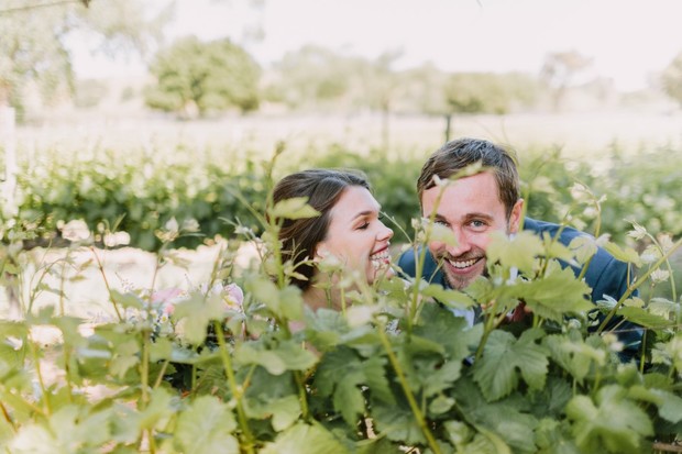 Happy couple peeking through vineyard plants smiling