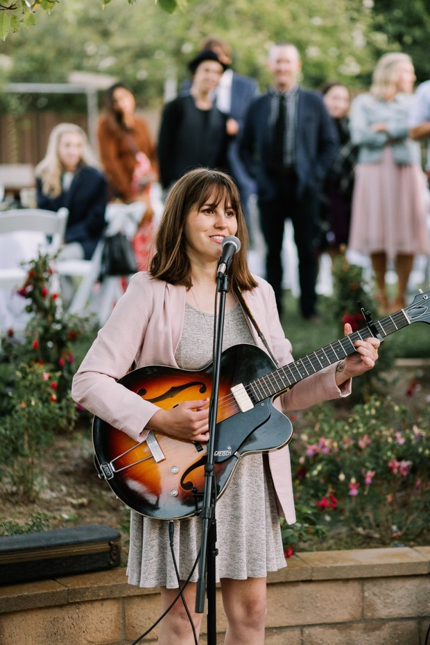 Woman plays guitar and sings at outdoor wedding venue