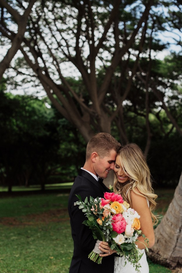 Bride and groom embrace with colorful bouquet outdoors