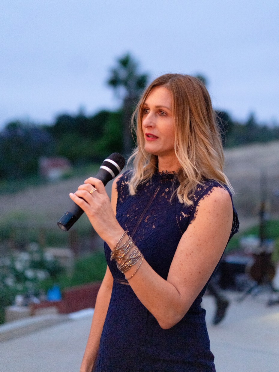 Woman in blue dress speaking at an outdoor event with a microphone