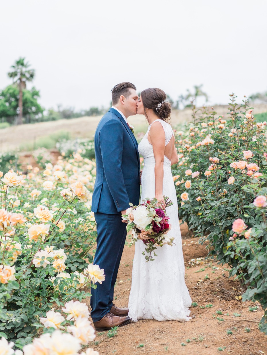 Newlyweds share a kiss in a garden of roses on their wedding day