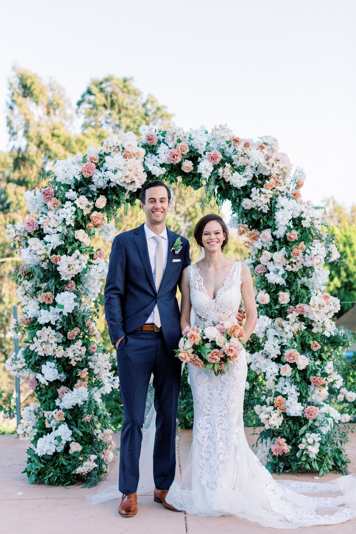 Newlyweds pose smiling under a floral wedding arch