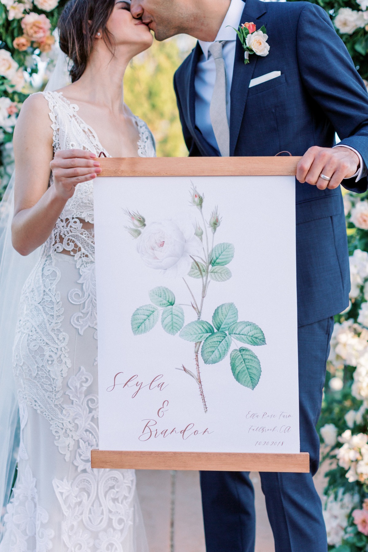Newlyweds kiss, holding a wedding sign with floral art